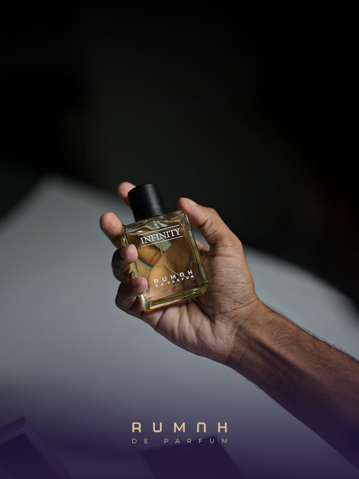 The amber Infinity bottle held in low light, its black cap in shadow