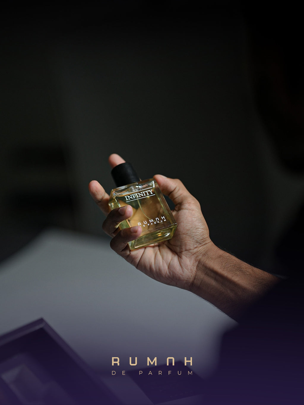 A hand holding the amber Infinity bottle against a dark background
